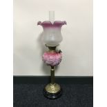 An early 20th century brass oil lamp with pink glass shade