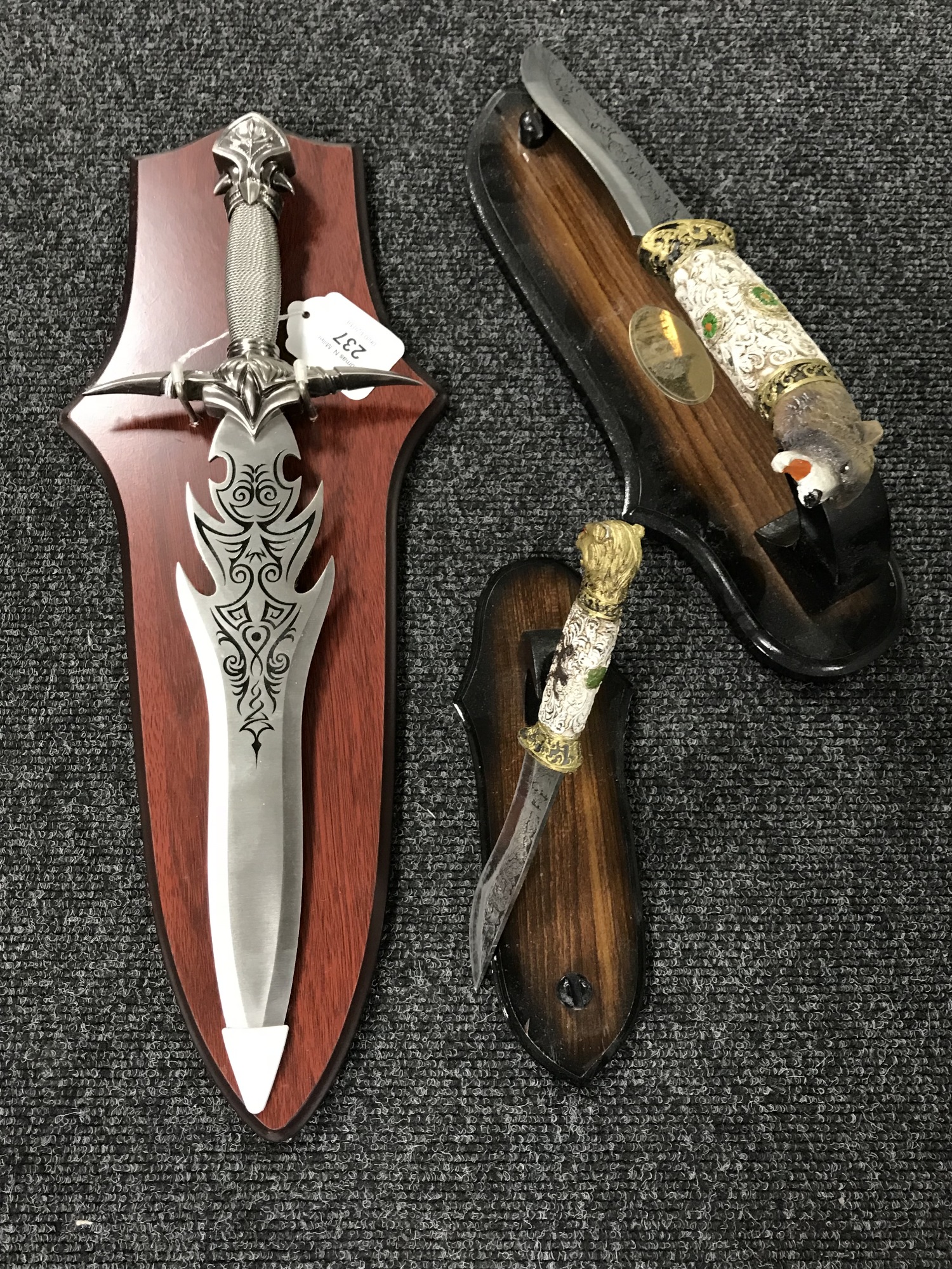 A fantasy knife on wooden shelf together with two hunting knives with animal grips on stands