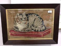 A nineteenth cetnury wool tapestry depicting a cat lounging on a red cushion, 48 cm x 31 cm, framed.