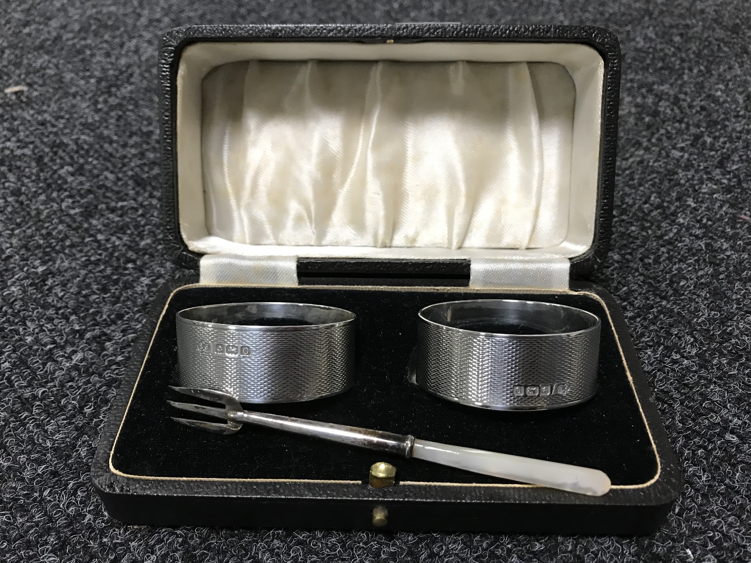 A pair of cased silver napkin rings together with a silver pickle fork