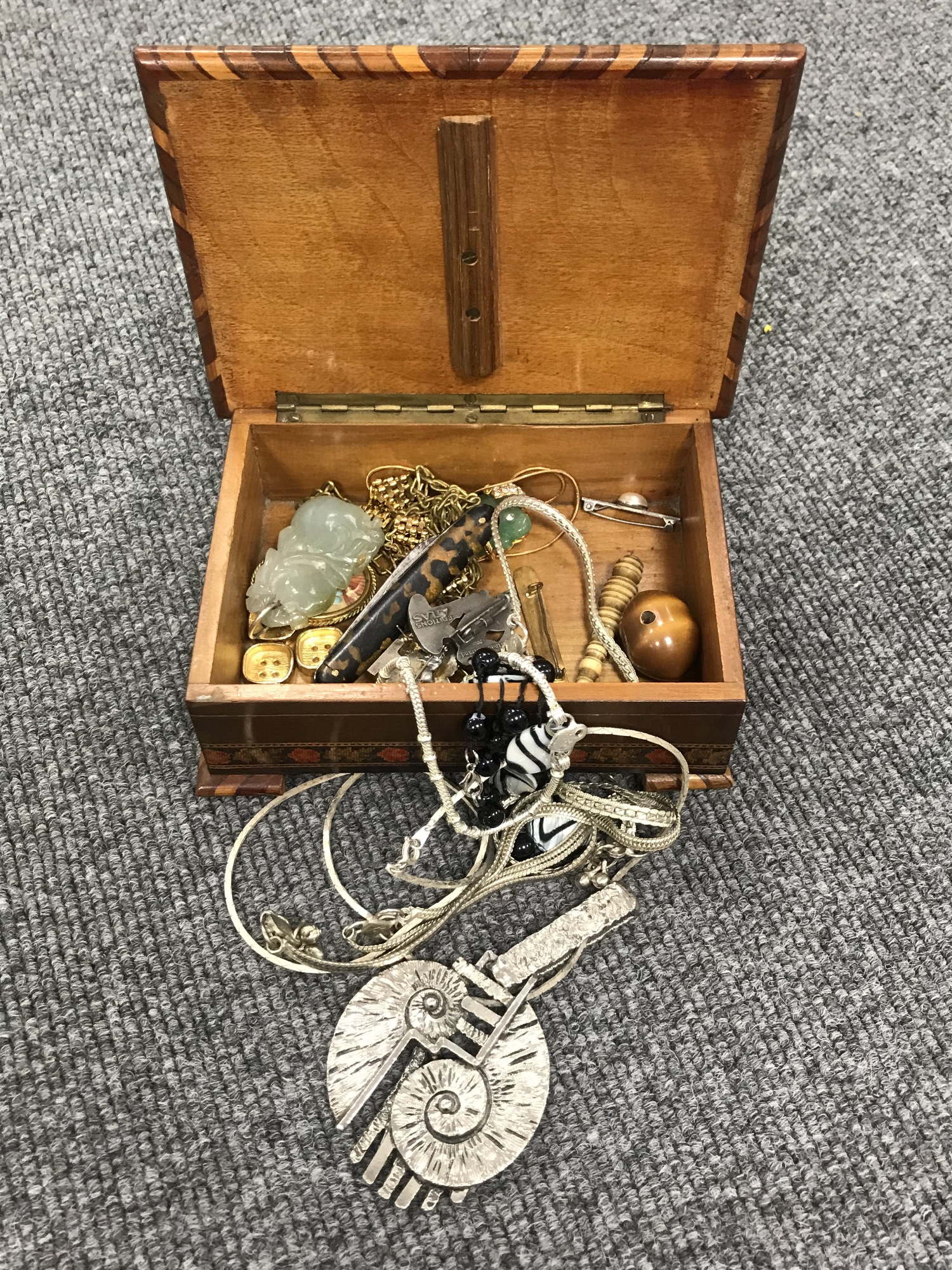 A wooden jewellery box containing assorted costume jewellery, including brooches, necklaces,