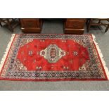 A fringed Indian rug on red ground,