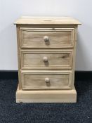 An unfinished pine three drawer bedside chest