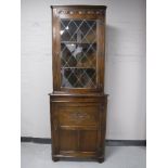 A carved oak corner cabinet with leaded glass door