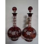A pair of cranberry glass decanters with leaf and grape decoration.