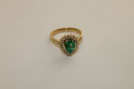 An 18ct gold emerald and diamond ring, a pear cut emerald within a border of brilliant cut diamonds,