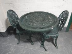 A cast metal circular patio table and two chairs