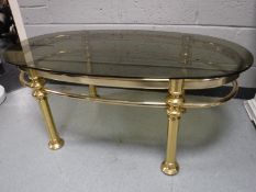 An oval brass coffee table with smoked glass top