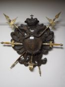 A carved oak coat of arms with ornamental swords and halberds