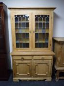 A blonde oak stained leaded glass door bookcase fitted cupboards and drawer beneath