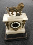 A Victorian alabaster mantel clock with enamelled dial surmounted by a lion on a wooden base