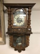An ornate oak cased wall clock with copper-surrounded hand painted dial,