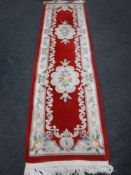 A Chinese fringed carpet runner on red ground,