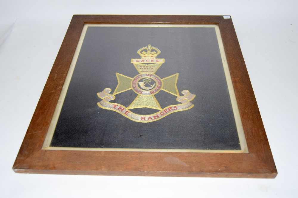 A framed and glazed woolwork embroidery of the badge of the 12th County of London Regiment The