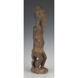 A Baule carved wooden male figure, Ivory Coast, modelled seated on a stool with parted legs, the