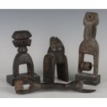 A group of four African carved hardwood heddle pulleys, one carved with overall masks in low relief,