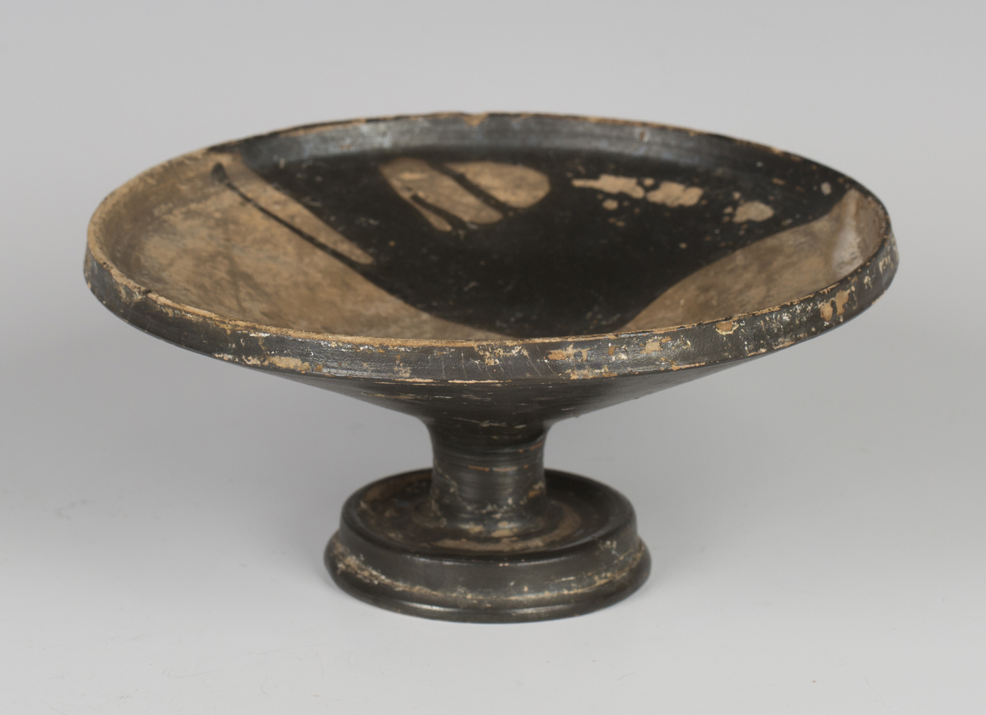 An Ancient Greek black painted terracotta kylix, approx 400BC, the shallow circular bowl raised on a