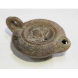 An Ancient Roman red earthenware oil lamp, the circular top decorated in relief with a mask,