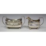 A George III silver two-handled sugar bowl and matching cream jug, each of cushion form with angular