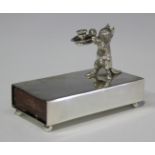 A late Victorian silver matchbox sleeve, mounted with a cat holding a chamberstick, raised on ball