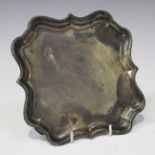 An Edwardian silver shaped square card salver with piecrust rim, on scroll legs, London 1902 by