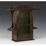 An early 20th century Arts and Crafts style stained walnut hanging wall cabinet, the galleried top