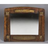 An early 20th century Arts and Crafts oak wall mirror, the shaped and arched frame inset with