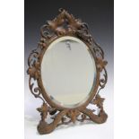 An early 20th century Swiss Black Forest carved softwood dressing table mirror, the oval bevelled