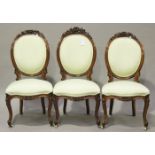 A set of three mid-Victorian walnut showframe salon chairs with carved foliate top rails, raised