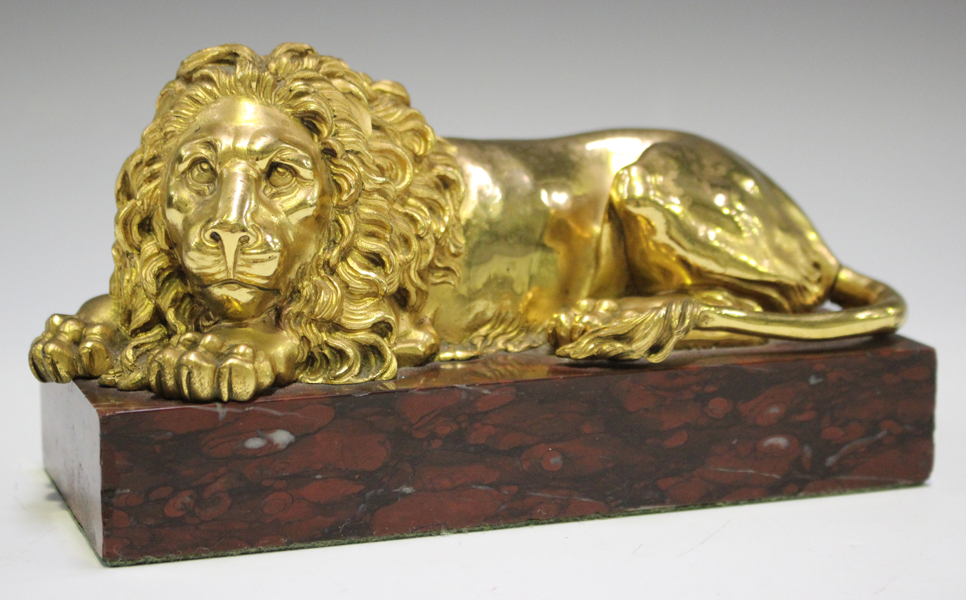 A late 19th/early 20th century gilded cast bronze model of a recumbent lion, on a rose marble