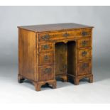 A George I walnut kneehole desk, the feather and crossbanded top above an arrangement of seven