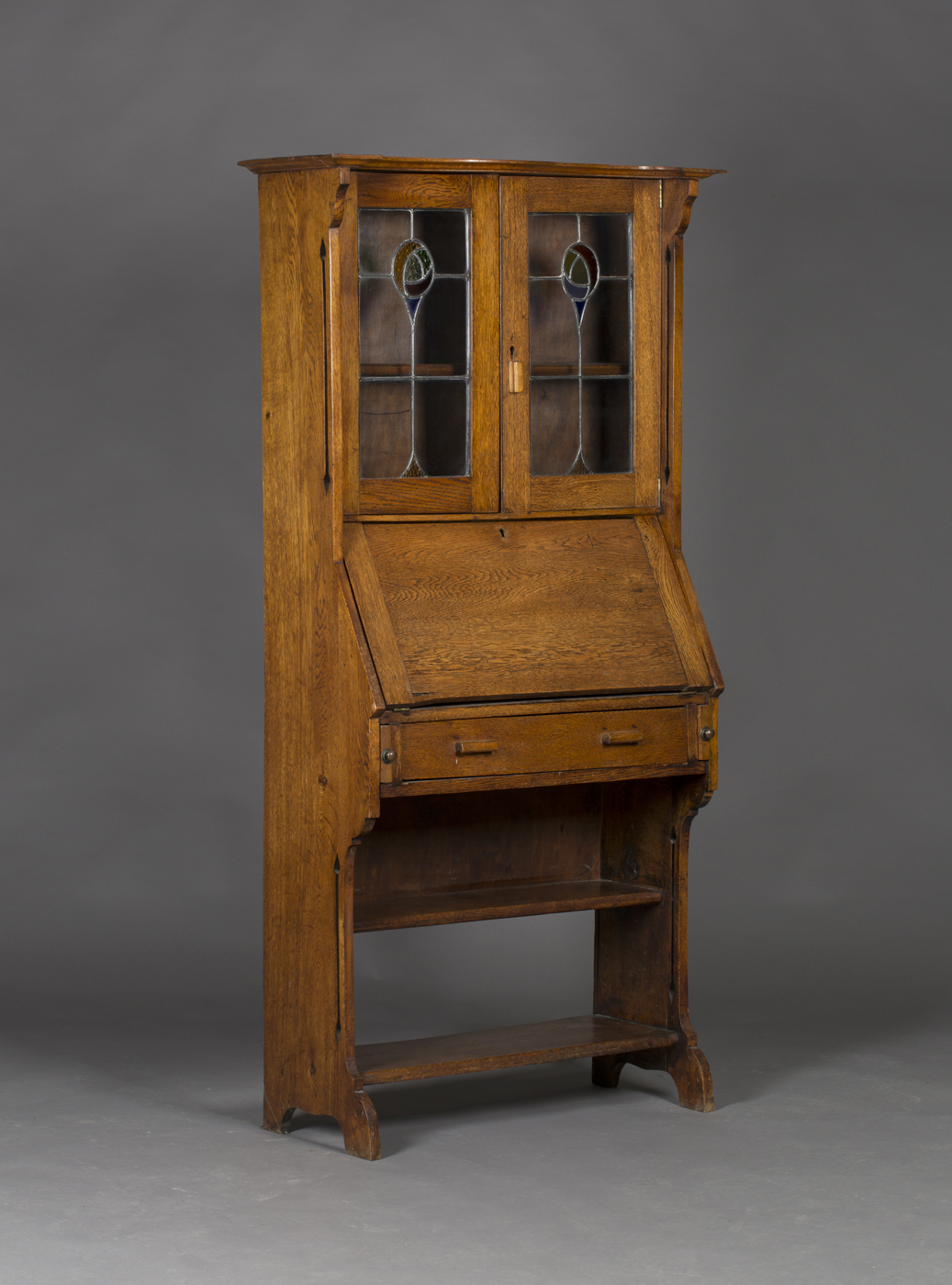 An Edwardian Arts and Crafts oak bureau bookcase, the canopy pediment above a pair of stained and