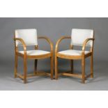 A pair of early 20th century oak framed elbow chairs by Heal & Son, the curved backs and seats