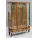 A pair of early 20th century walnut bowfront display cabinets, each with a moulded pediment above