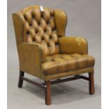 A late 20th century wing back armchair, upholstered in buttoned brown leather, on chamfered block