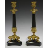 A pair of Regency style black patinated bronze and ormolu candlesticks, the reeded stems with