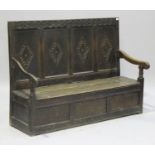 An 18th century oak settle with later carved decoration, the hinged seat above a panel front, on