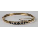 A 9ct gold, sapphire and diamond oval hinged bangle, mounted with a row of seven circular cut