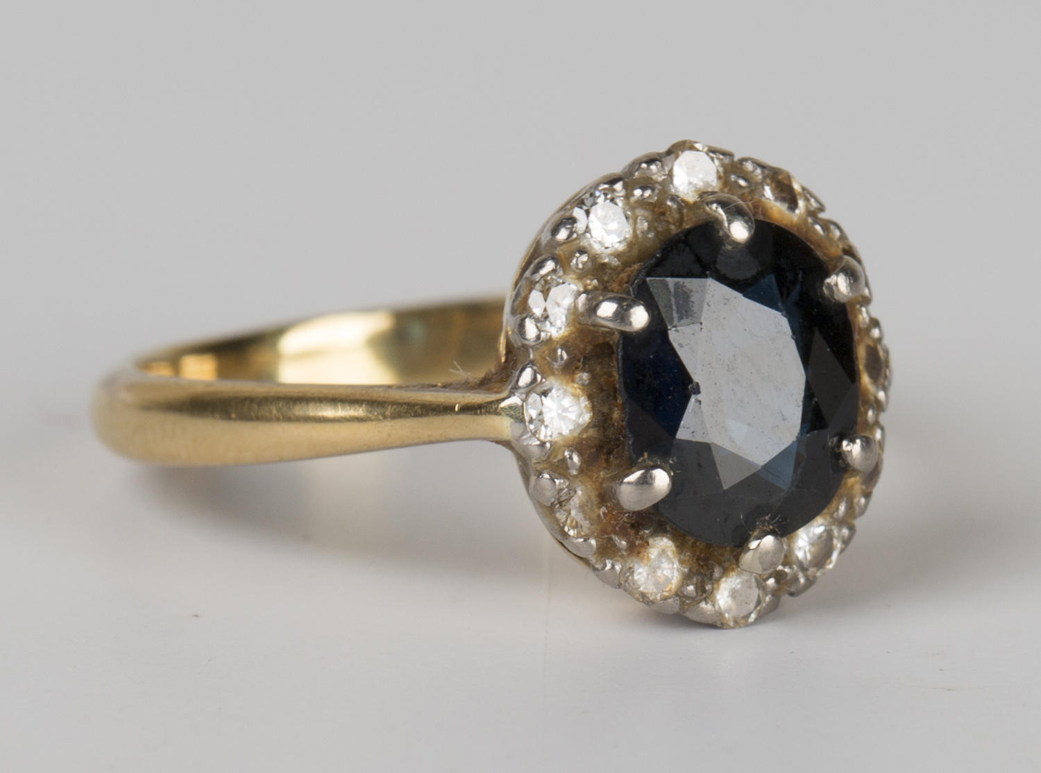 An 18ct gold, sapphire and diamond oval cluster ring, claw set with the oval cut sapphire within a