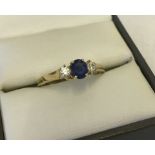 A 18ct gold dress ring set with central round sapphire and two diamonds either side.