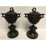 A pair of antique bronze lidded urns on marble bases.