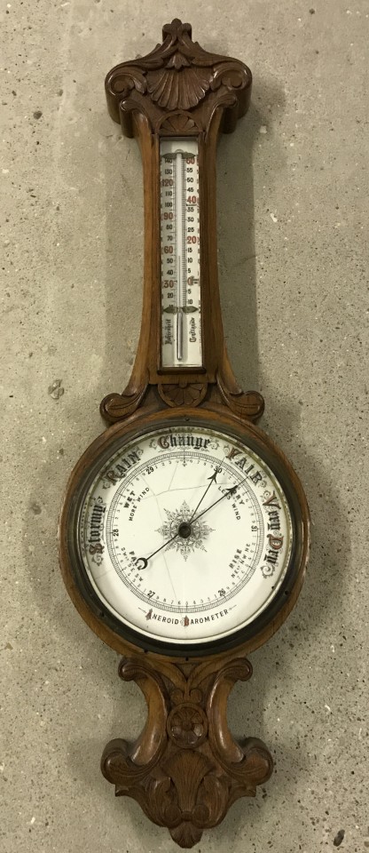 A vintage barometer with carved decoration and thermometer.