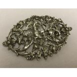 An ornate white metal brooch with a central cupid figure and grape and flower design throughout.