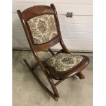 A vintage wooden frame folding rocking chair with tapestry upholstery.
