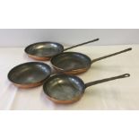 A set of 4 graduated copper frying pans with brass handles.