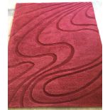 A modern rose red coloured wool carpet with cut out swirl pattern.