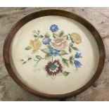 A vintage dark wood framed circular tray with glass covered floral design needlepoint base.