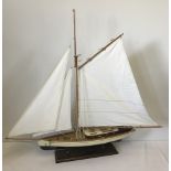 A modern model sailing boat mounted on a wooden plinth.