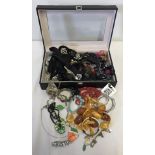 A large black leather effect box with clear lid, containing costume jewellery.