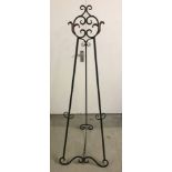 A modern black metal easel style display stand with scroll shaped detail to top and feet.